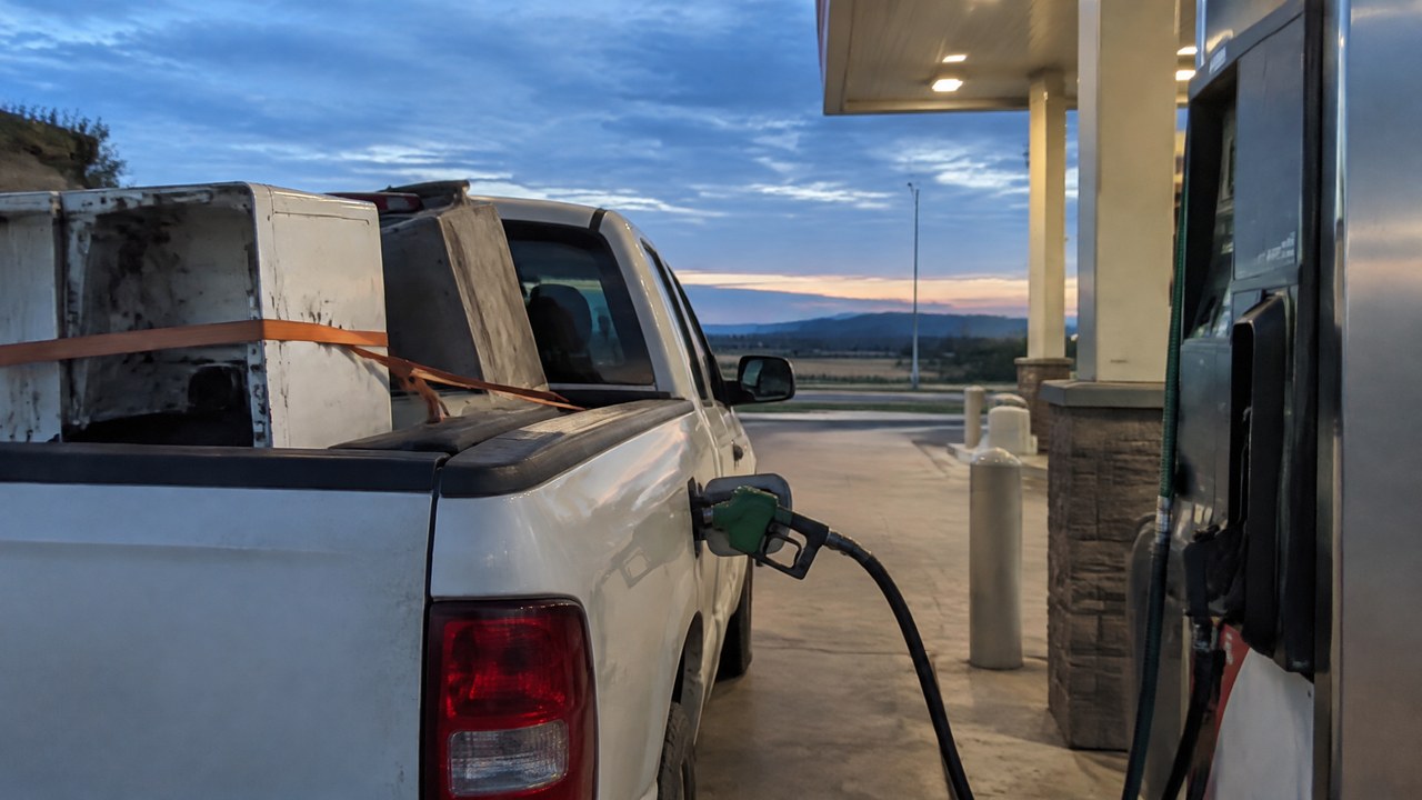 Pickup with scrap appliances strapped in the bed, filling up at a diesel pump at dawn