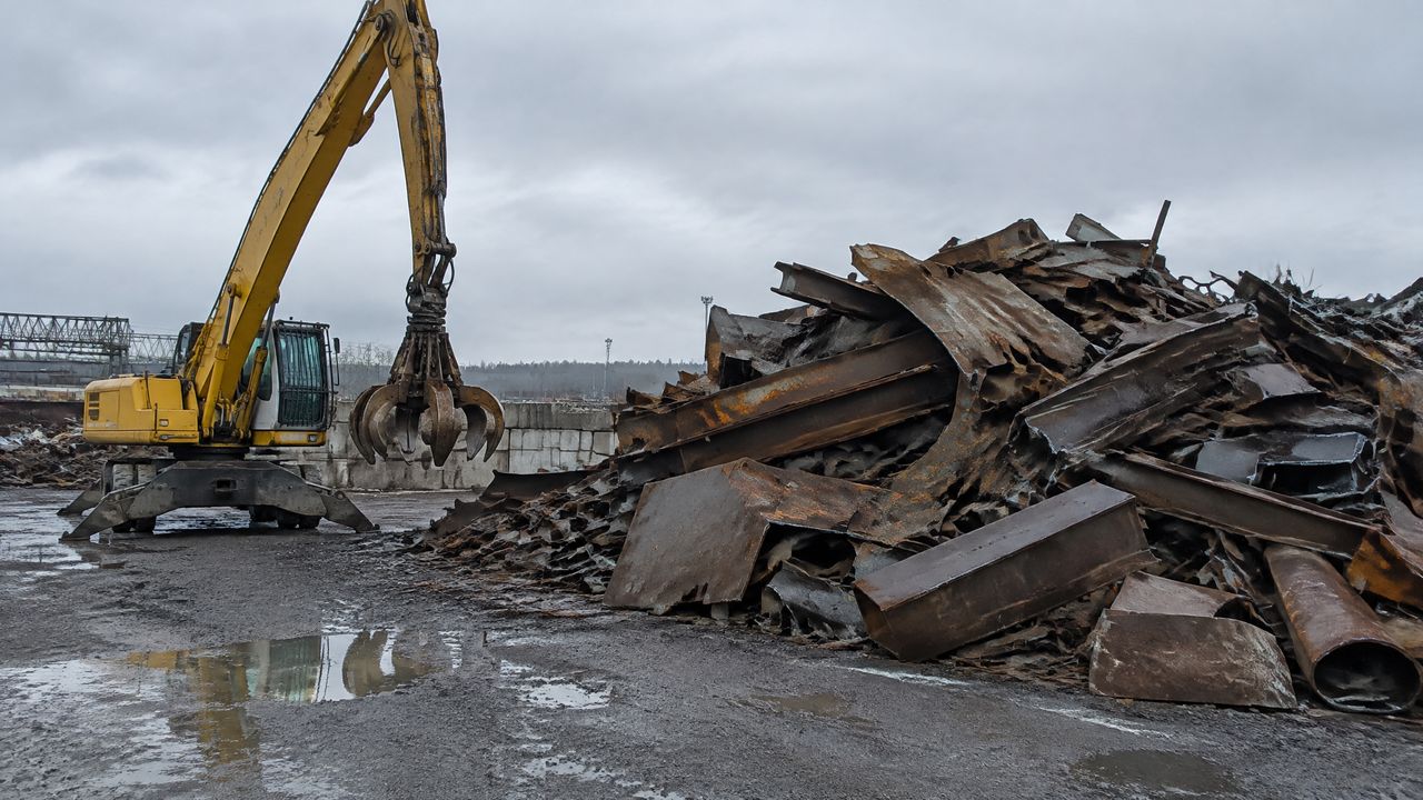 Pile of heavy melting steel with a grapple excavator beside it at a scrap yard